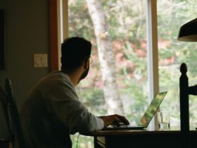 Man in gray hoodie using laptop while looking to the outside