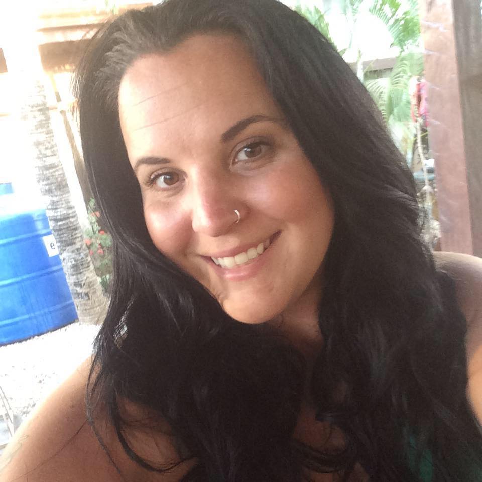 a woman with long wavy black hair and a nose ring stands smiling with a washed out background behind