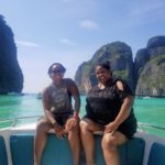 Corritta Lewis sits on the side of a boat with emerald green ocean and tall cliffs behind in Thailand