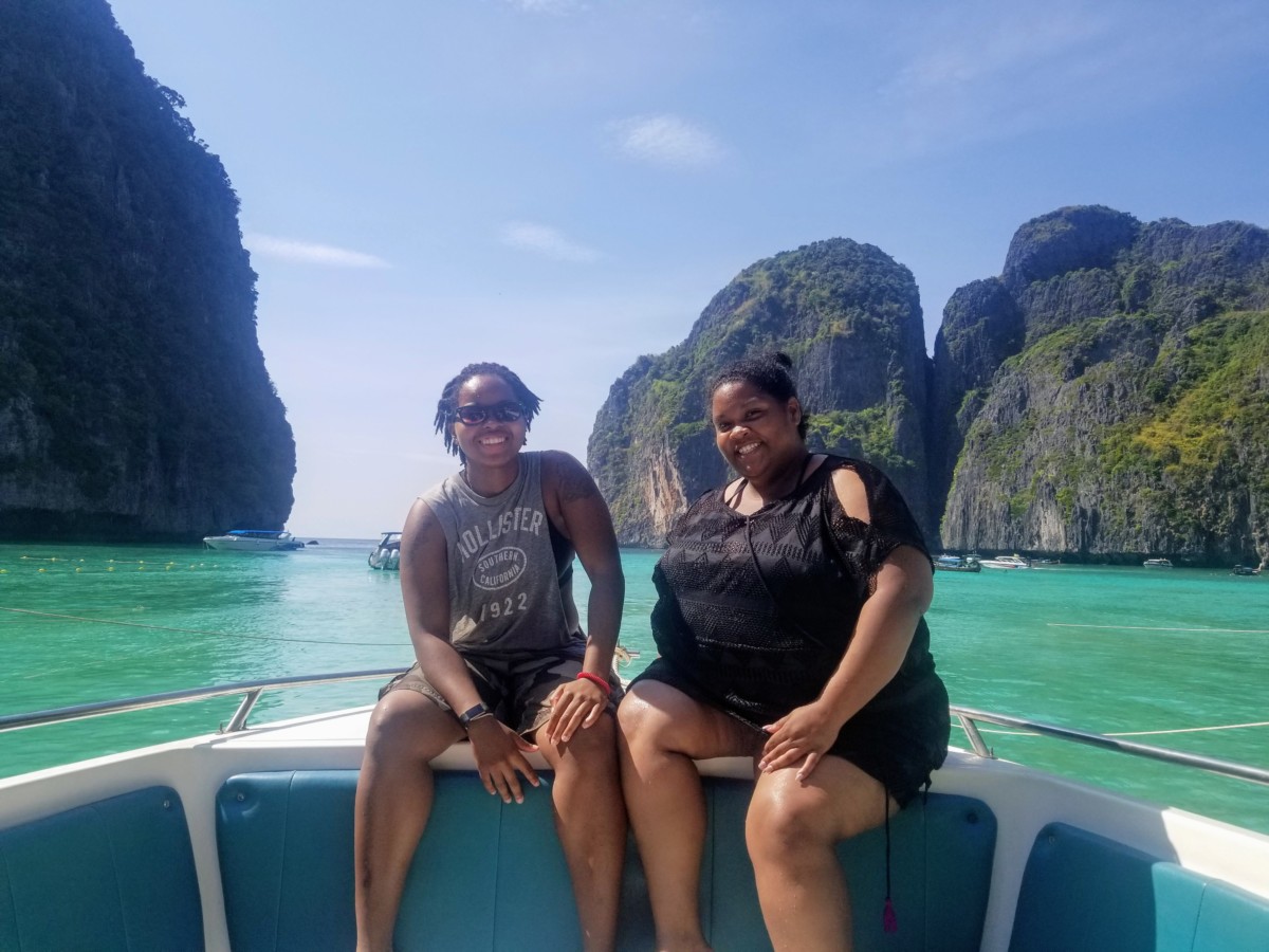 Corritta Lewis sits on the side of a boat with emerald green ocean and tall cliffs behind in Thailand