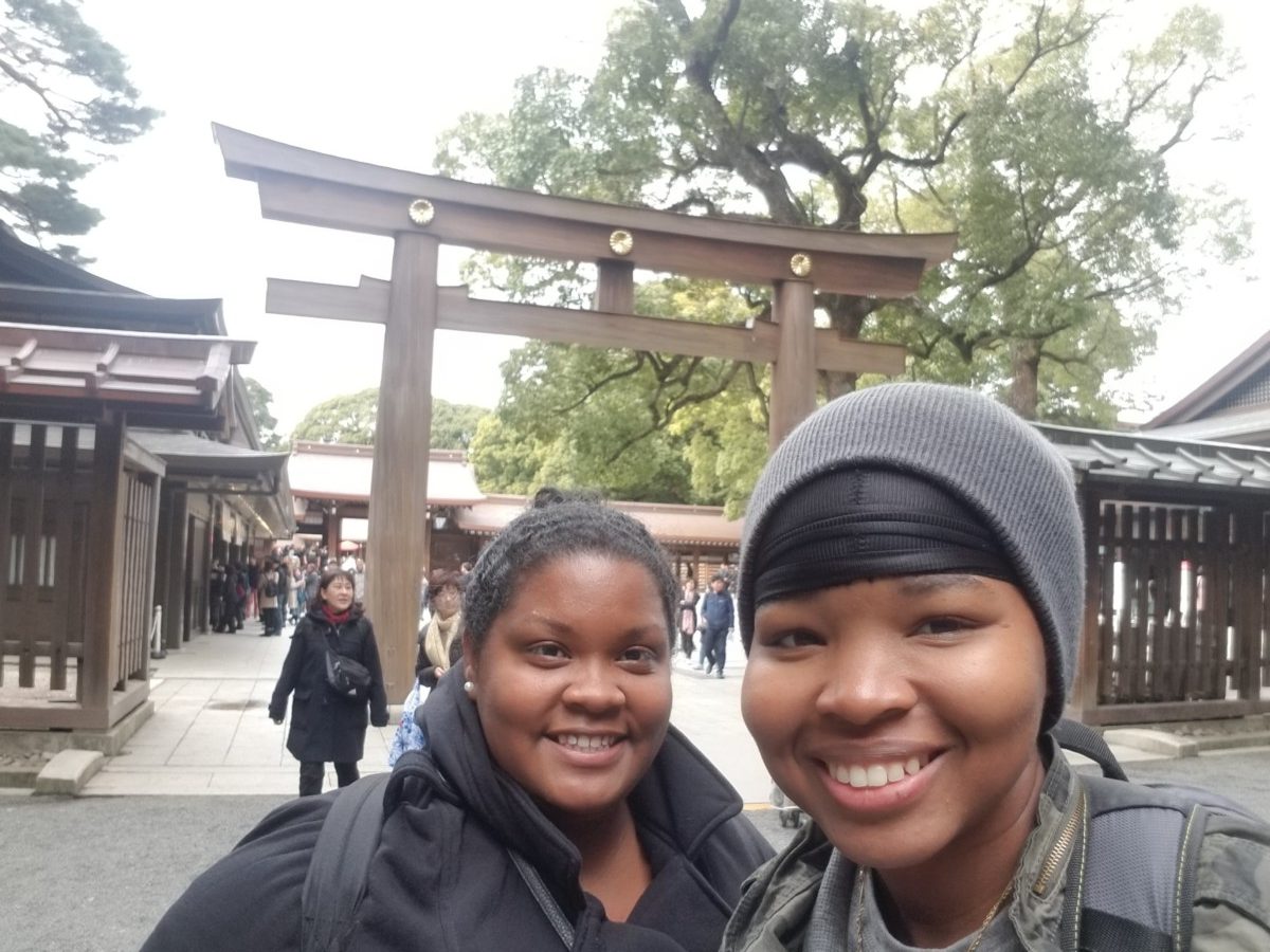 Two women stand near a tori gate in Japan on an overcast day