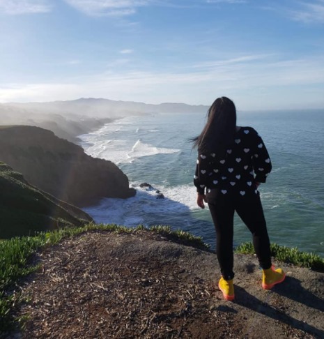 A women stands at the edge of a cliff overlooking the ocean below in San Francisco, California