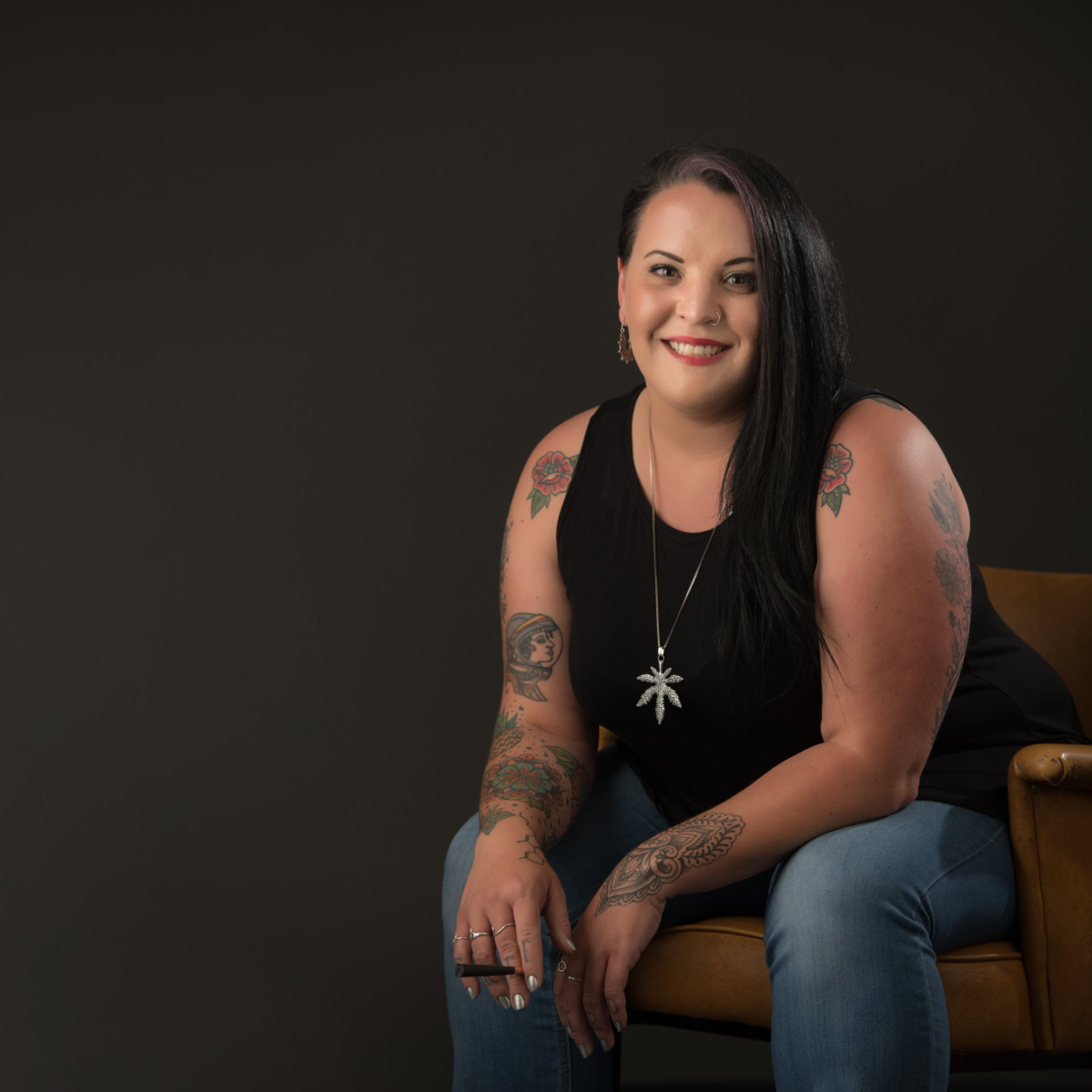 A woman sits slightly bent over with her elbows on her knees smiling to the camera