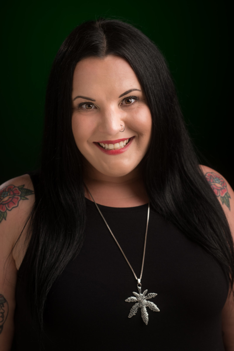 A professional photo of a woman wearing a black tank top with a long necklace and tattoos on her arms