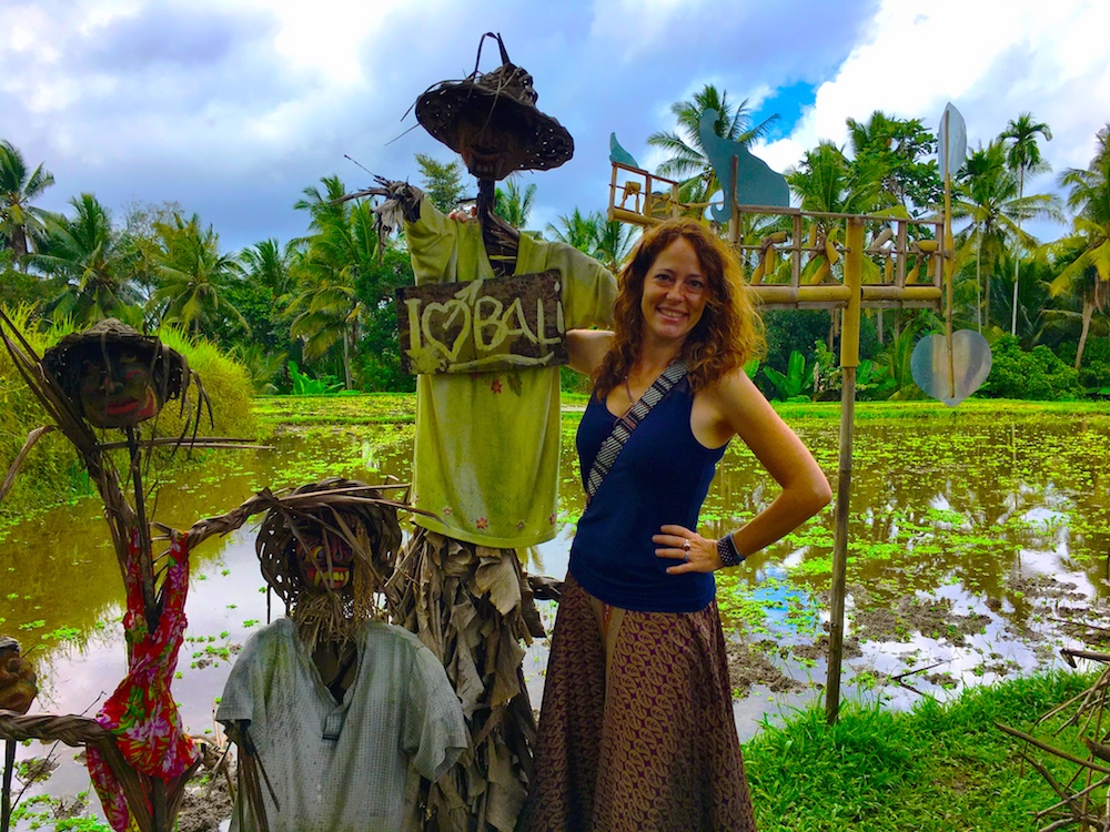 Nora Dunn stands near a flooded rice field next to a sign that says "I heart bali"