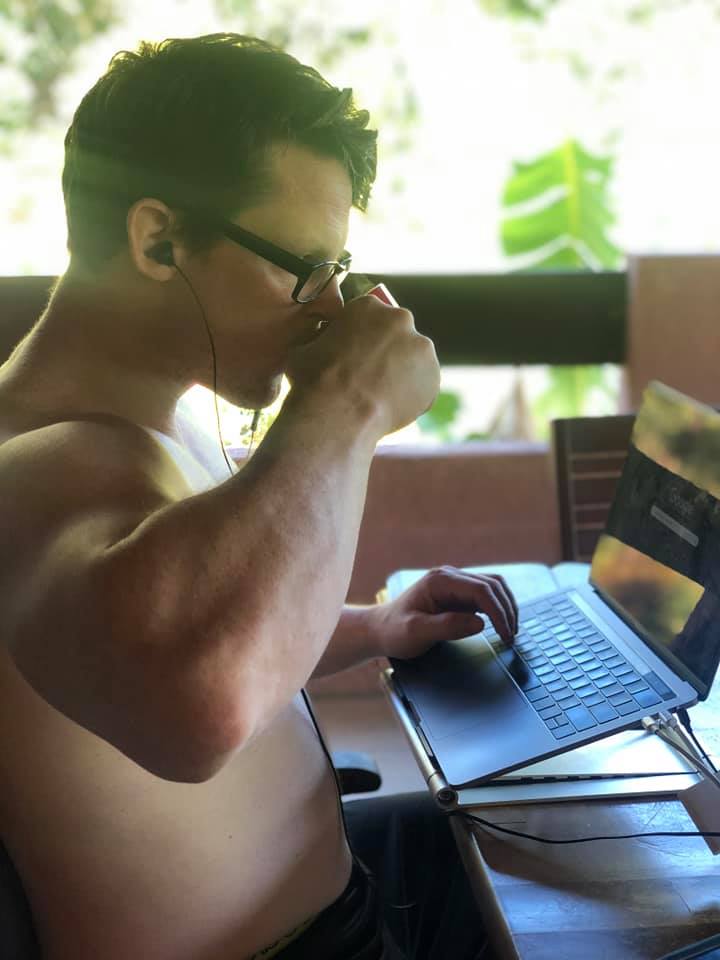 Loren ross sits in front of his computer working with his left hand while he drinks coffee from a mug in his right hand
