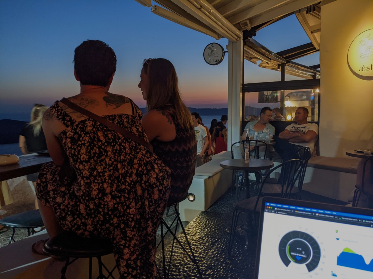 A man and a woman sit at a bar facing the sunset in Santorini, Greece