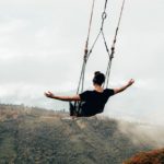 Blake Miner on a large swing with his arms out at his sides as he swings over a large valley