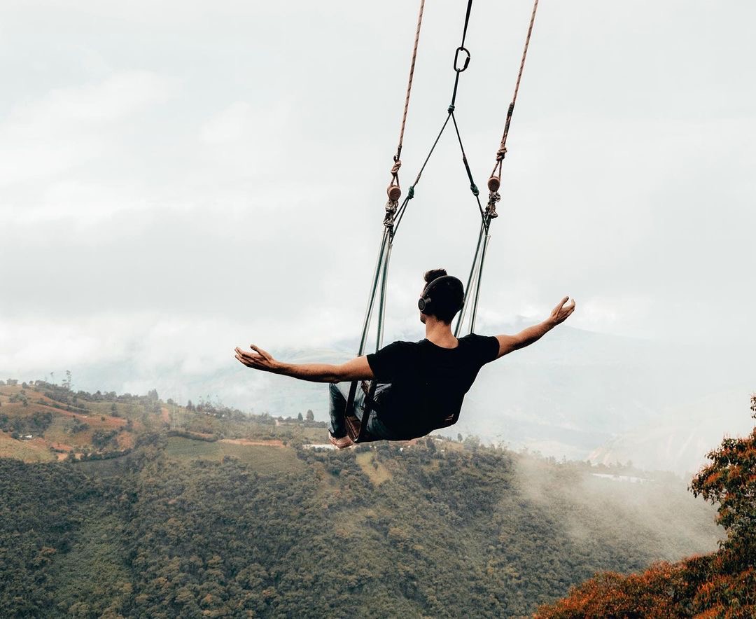 Blake Miner on a large swing with his arms out at his sides as he swings over a large valley