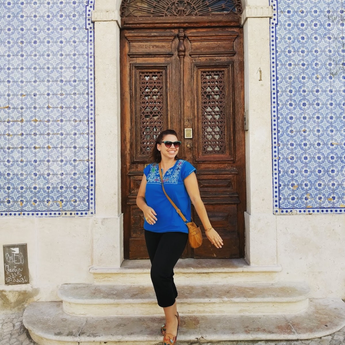 Lolly stands in front of a wooden door in Lisbon where walls on both sides of the door are covered in classic Portuguese blue tiles