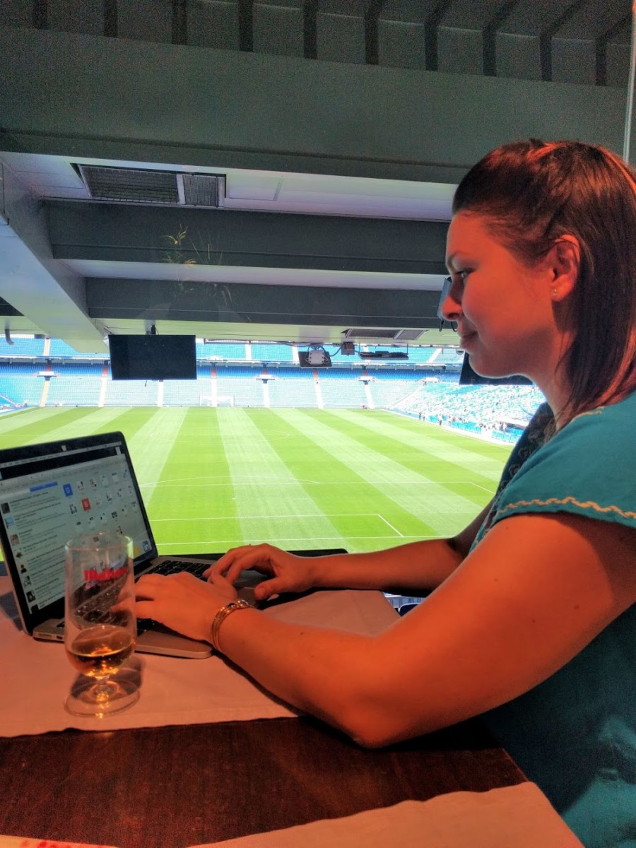 Lolly sits at a desk working on her computer at the Santiago Bernabeu in Madrid while a grass sports field is off to her right