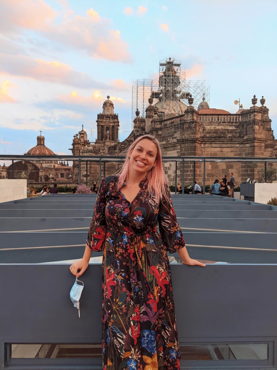 Lolly stands in front of a grand building in Mexico city with scaffolding on the highest part of it