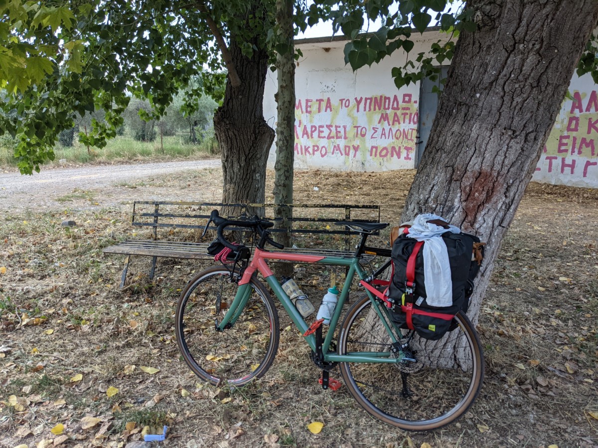 A red and green bicycle stands up against a tree in front of a building with Greek writing on it