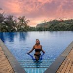 Anna stands at the base of a set of stairs in a pool with her arms by her sides touching the surface of the water