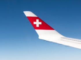 The wing of a swiss air flight in the sky with a few clouds below