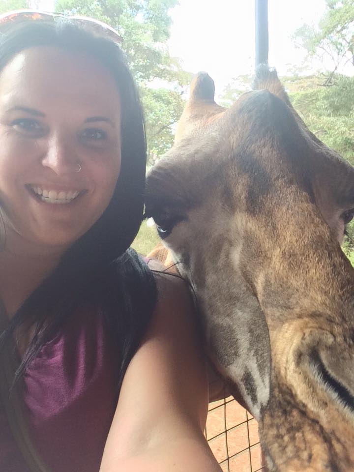  A close up of a woman next to a giraffe's head
