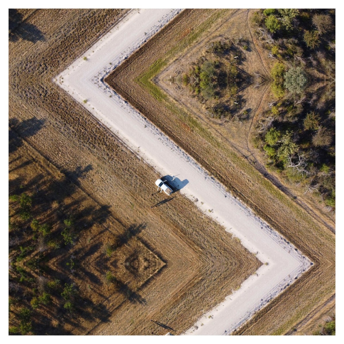 a photo of mirrored drone images creates a white zig zag road through a light green field