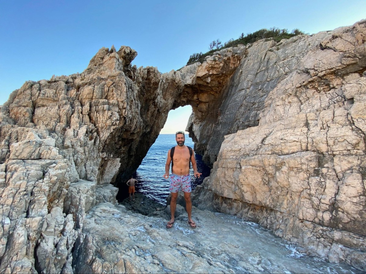 Dirk Bruwer stands under anaturally formed arch in a rock with the ocean directly behind the rock formation