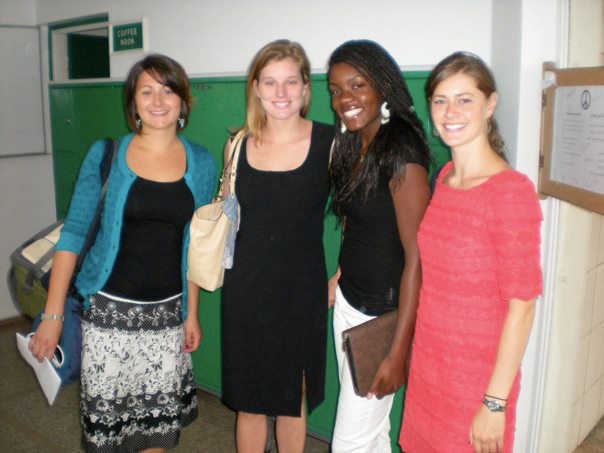 A group of four females stand in a line smiling dressed up for an event