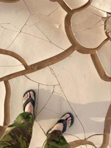 Dirk Bruwer takes a photo of his knees and feet with flip flops on in the desert in Africa where the ground has huge cracks in it from drying out