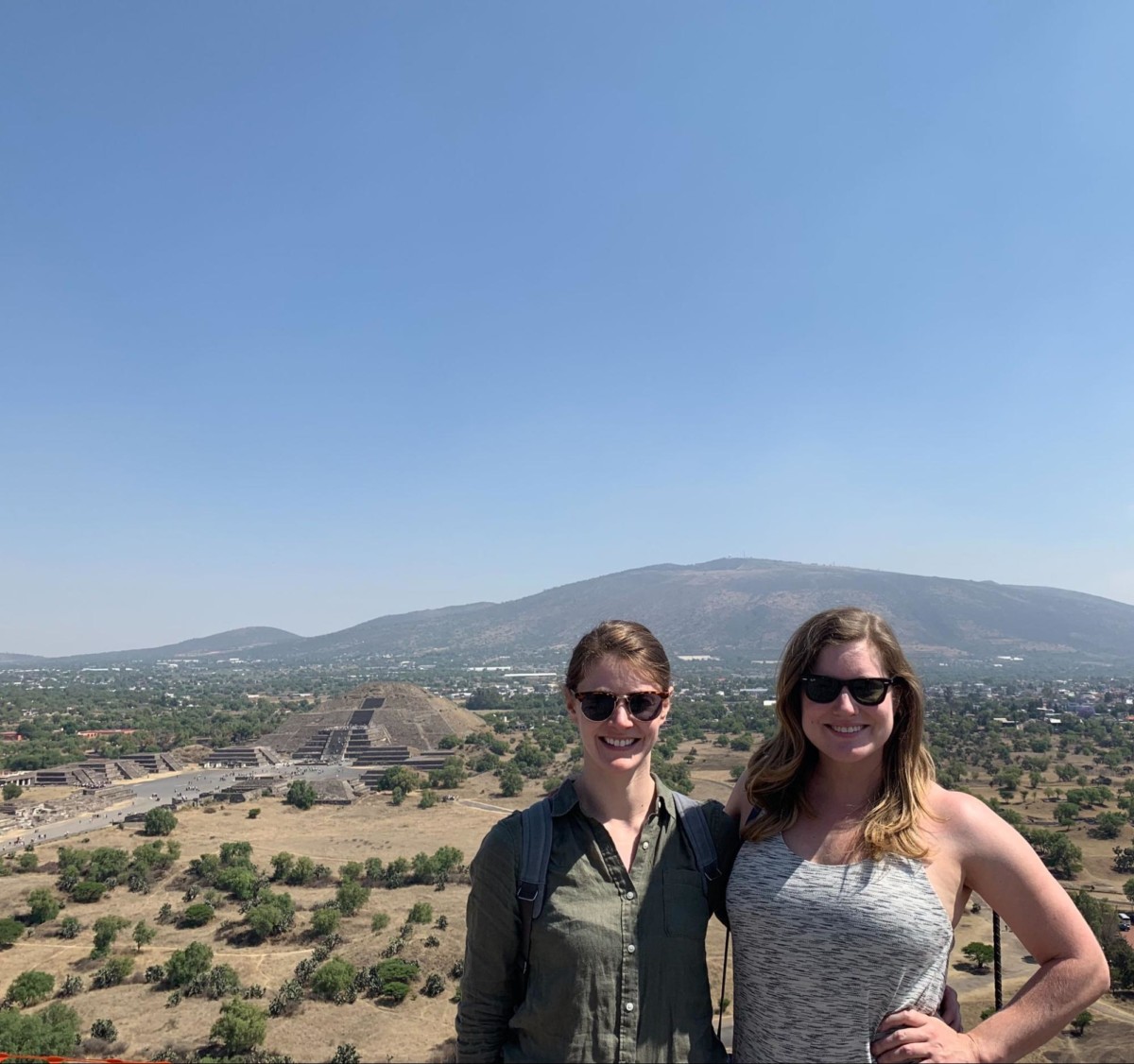 Katherine Conaway stands arm and arm with a female friend in a desert covered with occasional green scrub plants