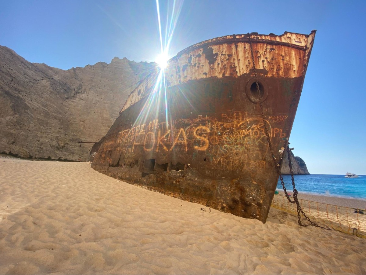 An old rusted boats sits on a sandy shore in Namibia with the sun shining over it and the ocean off the the right