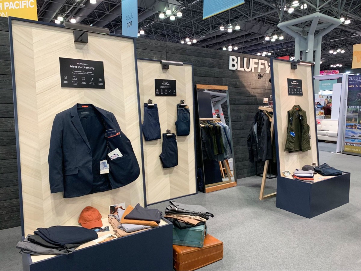 A display of clothing at a trade show shows a blazer hanging in the foreground with a pants display in the center and a vest on the right