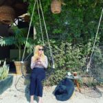 mary blackiston sits on a swing looking left while holding a coffee in both hands