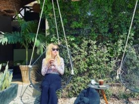 mary blackiston sits on a swing looking left while holding a coffee in both hands