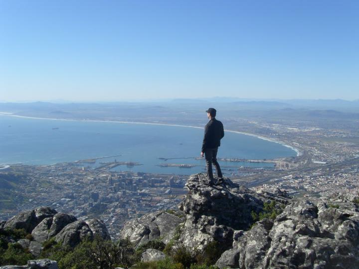 Blake Miner stands on a rocky ledge overlooking a bay and a city in South Africa