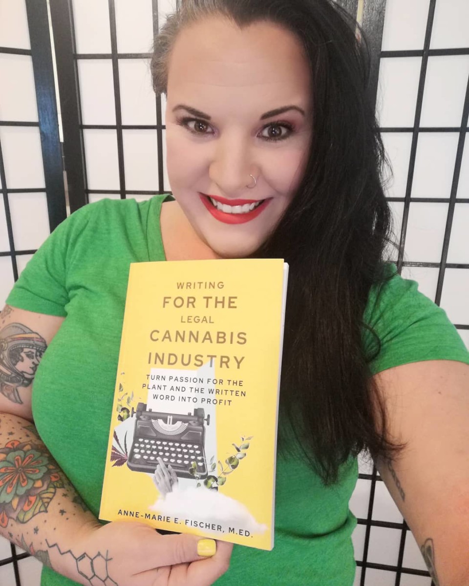 A woman stands holding a book she wrote called "writing for the legal cannabis industry"