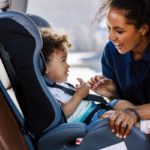 African American woman fastening her child to a denim blue car seat