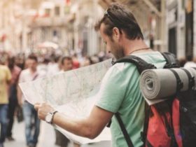 Caucasian guy carrying a red backpack with a yoga mat holder navigating an unfamiliar city with a map