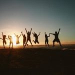 Silhouettes of 11 friends taking a jump shot in front of the ocean during sunset