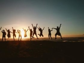 Silhouettes of 11 friends taking a jump shot in front of the ocean during sunset