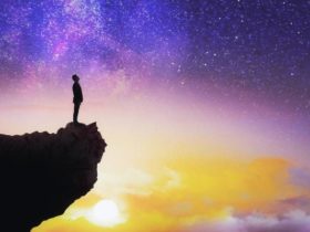 Silhouette of young man gazing at the northern lights while standing at the edge of the cliff