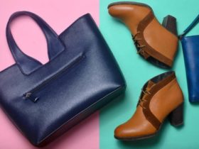 A travel garment bag on the floor beside a pair of brown ankle boots and a dark blue purse